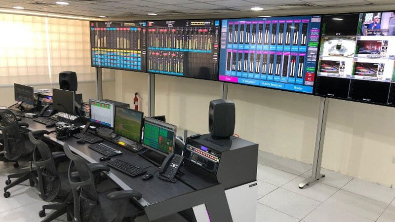 Bahrain radio control room includes audio level meter monitoring, video monitoring, telephone hybrid, router control panel, and desktops.