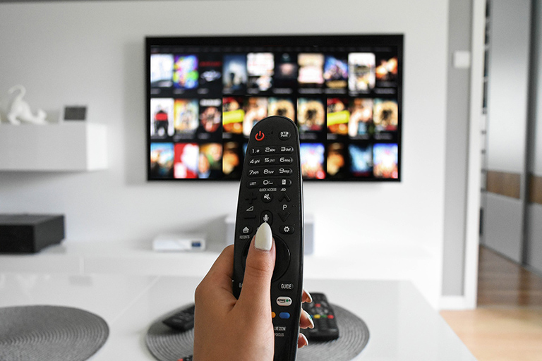 Hand holding remote control, navigating video on demand services on Television via an OTT platform.