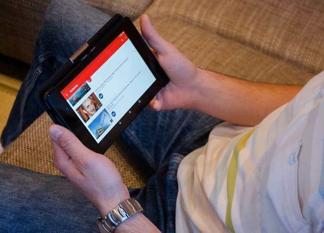 A man using a tablet to access an OTT platform, enjoying a personalized list of content recommendations generated by an AI-powered recommendation engine.
