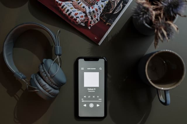 A headset placed near a smartphone, with a podcast being streamed, showcasing the popularity of podcasting and mobile consumption in the radio industry.