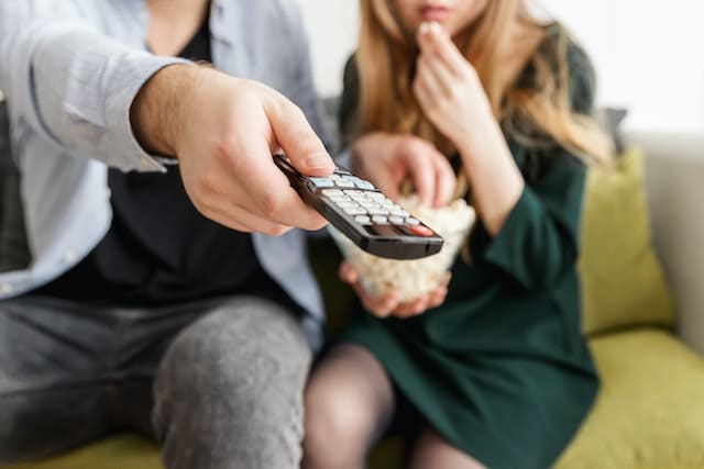 An image illustrating the concept of new trends in television, featuring a handheld remote control and a couple streaming content over their television, capturing the essence of modern viewing habits and the evolving landscape of television consumption.
