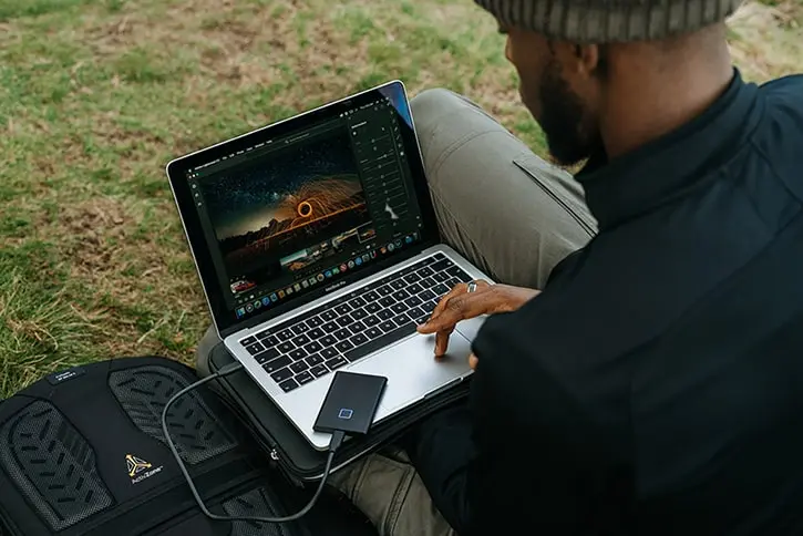 A professional working on a laptop with connected SSD for media storage.